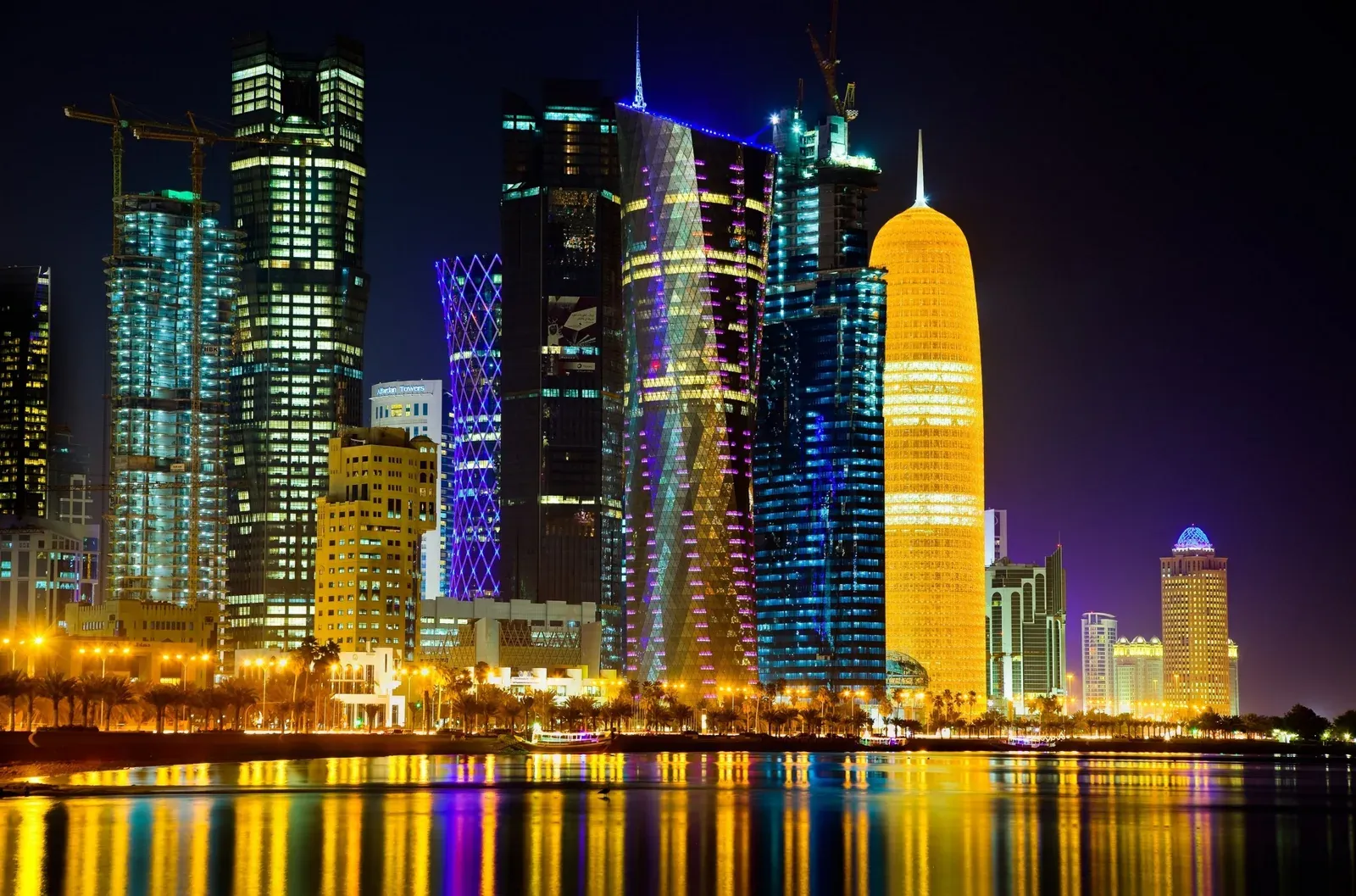 The Doha skyline at dusk seen across the bay with a traditional dhow in the foreground, Qatar