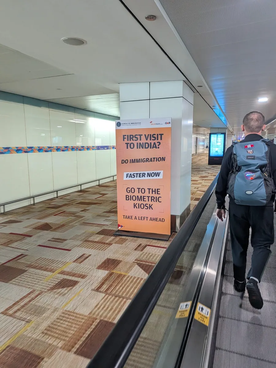 Bureau of Immigration sign in the Delhi T3 arrivals corridor: First visit to India? Do immigration faster now. Go to the biometric kiosk.